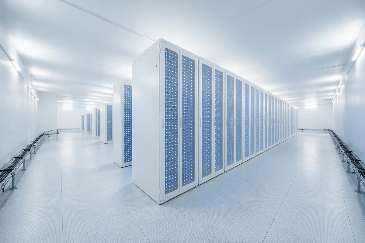 A completed row of high-density GPU cabinets in a bright white data hall, doors closed and status lights running the length of the row.